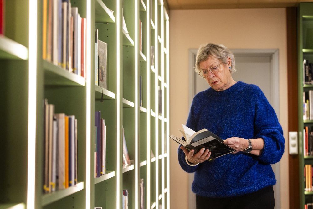 Eldre dame på bibliotek som leser en bok