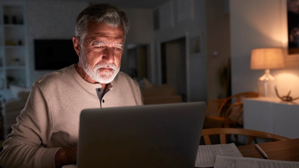Eldre mann i mørekt med laptop