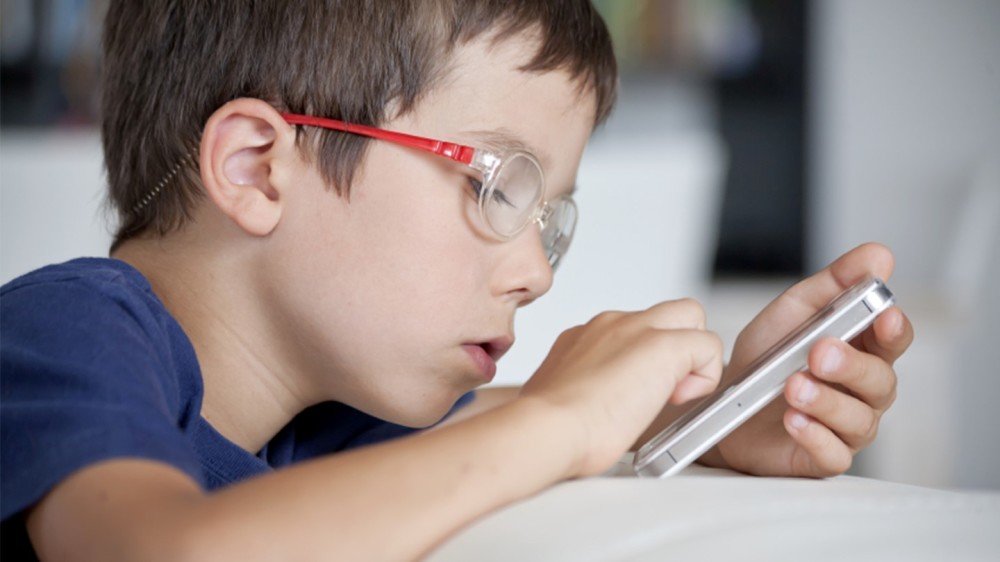 Ung gutt med briller som leser på mobil