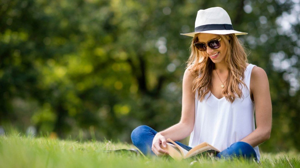 Ung dame med solbriller leser bok i parken